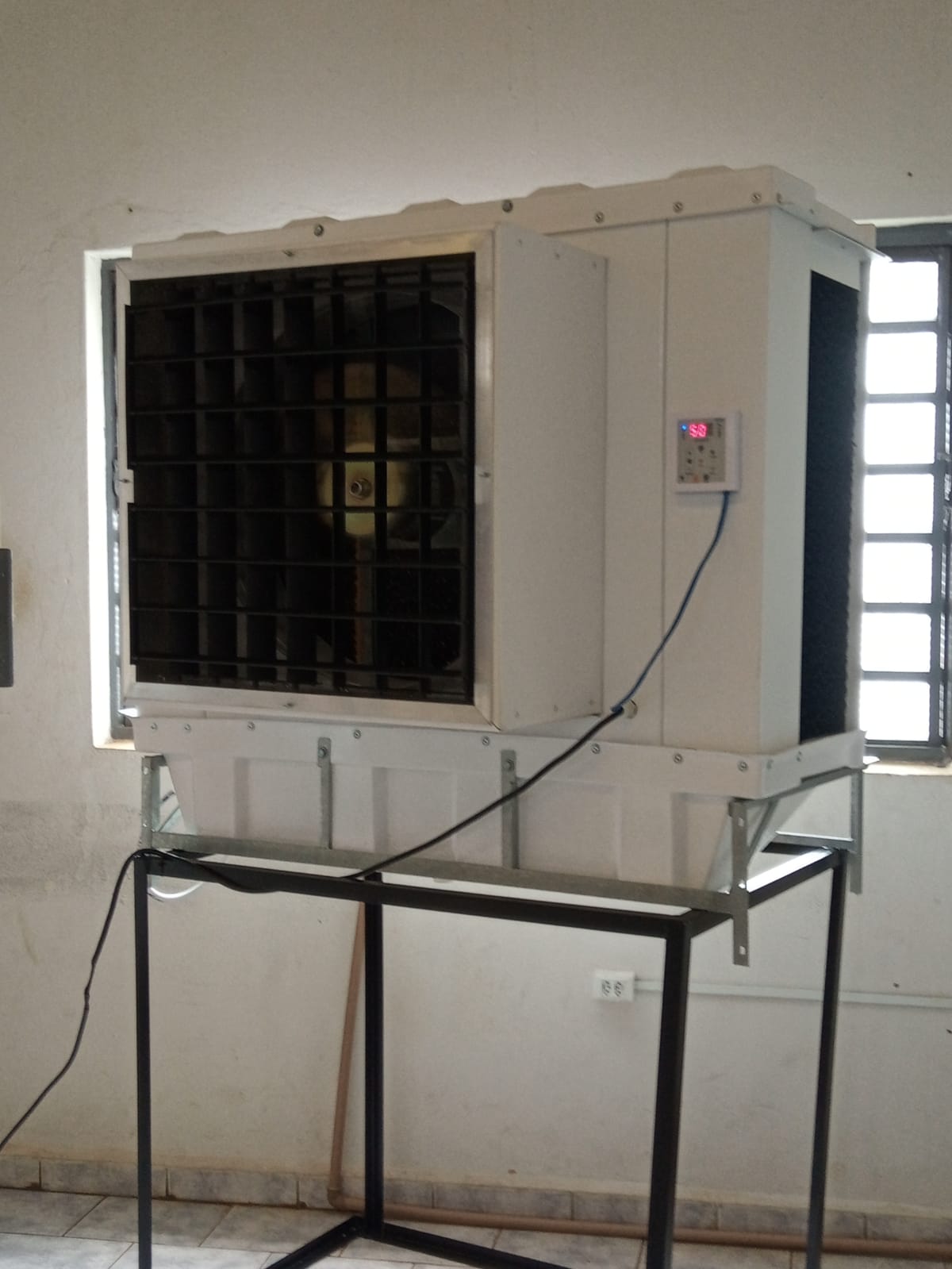 Unidade sobre suporte metálico dentro de uma sala, com o painel digital ligado.